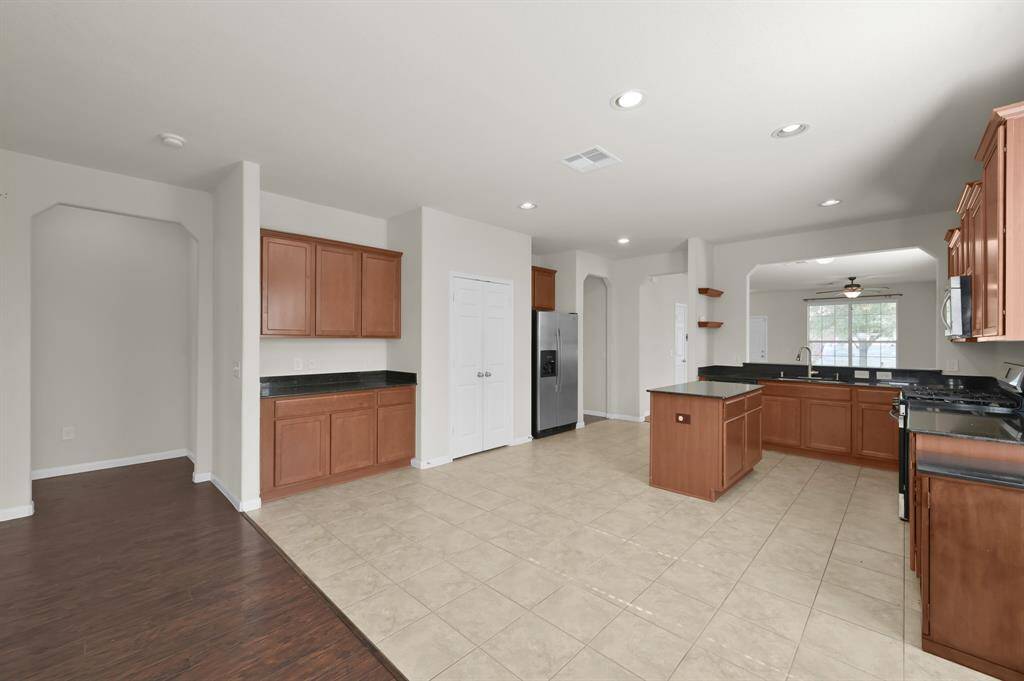 This room features hardwood floors, neutral walls, and ample natural light from two large windows. It includes a ceiling fan, a built-in desk unit, and wall space for a mounted TV.