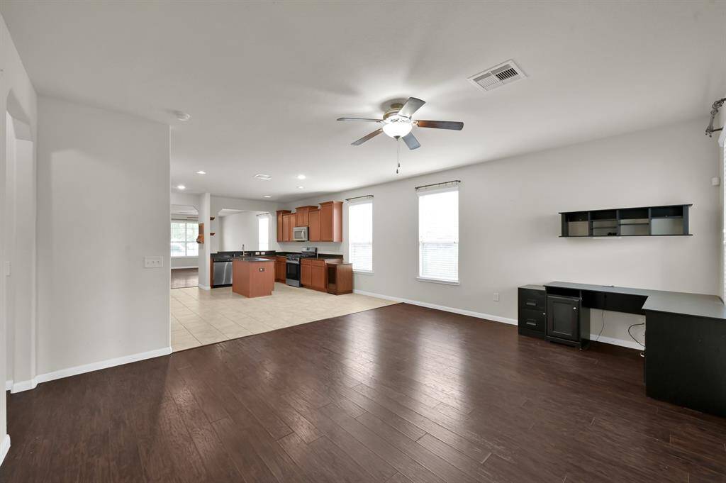 This room features hardwood floors, neutral walls, a ceiling fan, and two large windows offering natural light and a view of the backyard. It's spacious and versatile, perfect for a living area or office.