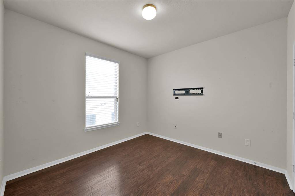 This room features hardwood flooring, neutral walls, and a ceiling light. It includes a double-door closet and additional door access, offering a simple and versatile space.