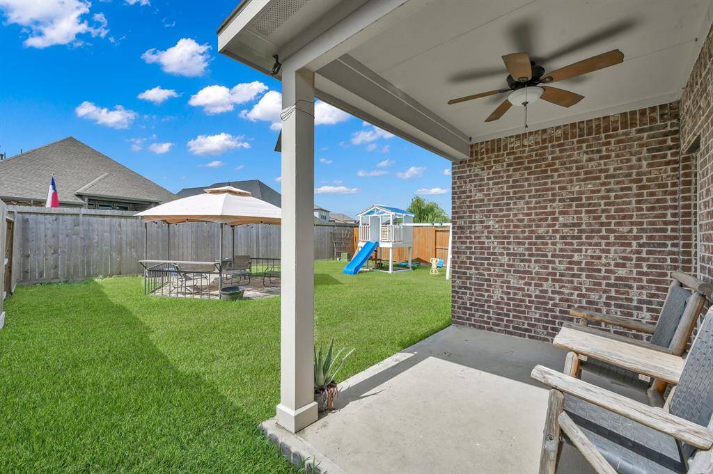 Spacious backyard featuring a lush green lawn, a playset with a slide for children, and a cozy patio area with a canopy for outdoor dining and relaxation. Ideal for family gatherings and playtime.