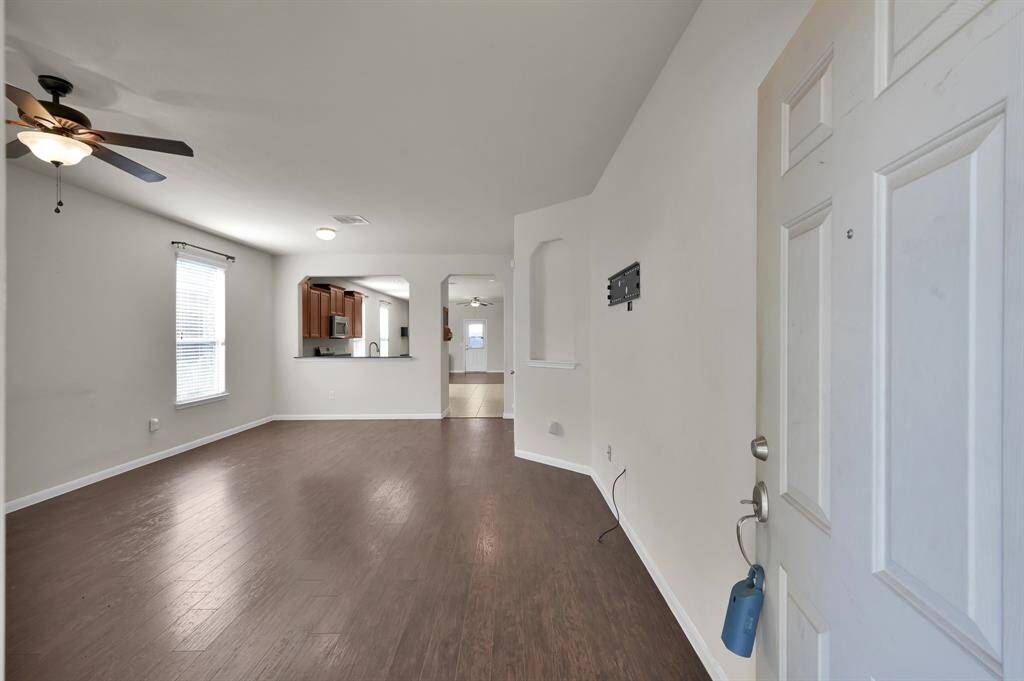 This photo showcases an open-concept living area and or living/dining combo with hardwood floors and neutral walls. The room features a ceiling fan, large windows for natural light, and a view into the kitchen with modern cabinetry. Perfect for family gatherings and entertaining.