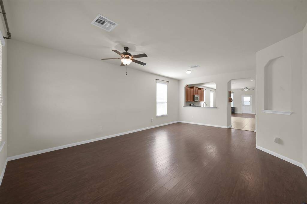 This spacious living area features hardwood floors, a ceiling fan, and neutral walls. It opens to a kitchen with a pass-through window, creating a seamless flow for entertaining.