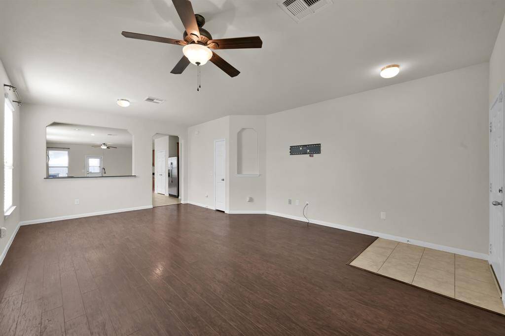 Living area features dark wood flooring, a ceiling fan, and neutral walls. It flows into an open kitchen with a pass-through window, creating a bright and inviting space.