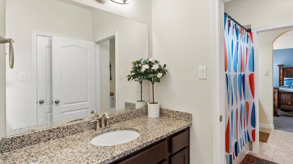 This bathroom boasts a sleek granite countertop with an undermount sink, modern fixtures, and a large mirror that enhances both style and functionality.