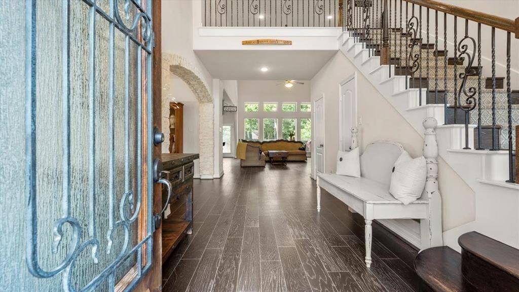 This inviting entryway features elegant wood flooring and a stylish staircase with wrought iron railings. The open layout flows into a bright living area with large windows, offering a welcoming and spacious atmosphere.