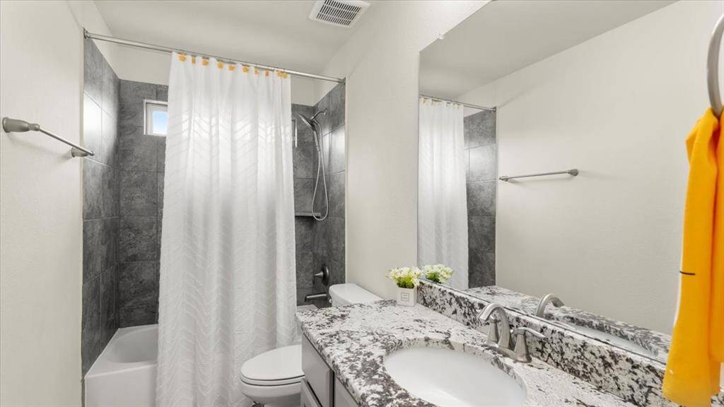 This bathroom showcases a modern design with granite countertops, generous counter space, and a shower-tub combo accented by a dark tile surround for a sleek, contemporary look.