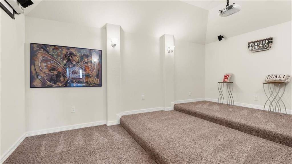This cozy home theater features tiered carpeted flooring, wall sconces that provide ambient lighting, and a ceiling-mounted projector—creating an inviting and immersive space for entertainment.