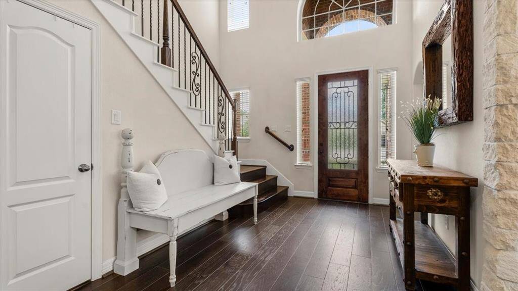 Step into a bright, open foyer featuring rich dark hardwood floors and a striking staircase adorned with elegant wrought iron railings. A cozy sitting area offers a warm welcome and flows effortlessly into a spacious living room, bathed in natural light from expansive windows.
