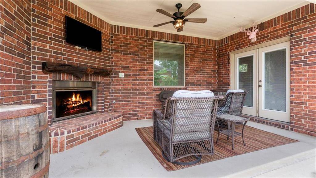 The cozy outdoor patio boasts a warm brick fireplace, space for a mounted TV, and comfortable seating. Equipped with a ceiling fan and French doors, it offers the perfect setting for relaxation and entertaining year-round.