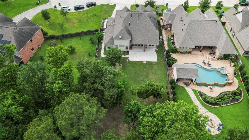 This aerial view highlights the generous size of the lot, featuring a spacious backyard nestled against a lush wooded area for added privacy. The property includes a patio and ample green space—offering excellent potential for outdoor amenities such as a pool or gardens, making it ideal for recreation and relaxation.