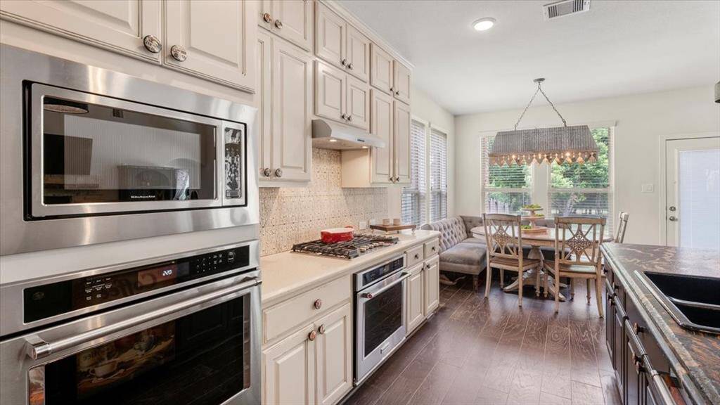 The kitchen is equipped with sleek stainless steel appliances, a gas cooktop, and a built-in microwave. White cabinetry contrasts beautifully with the dark hardwood floors, while a charming breakfast nook with large windows invites abundant natural light—creating a warm and inviting space to start your day.