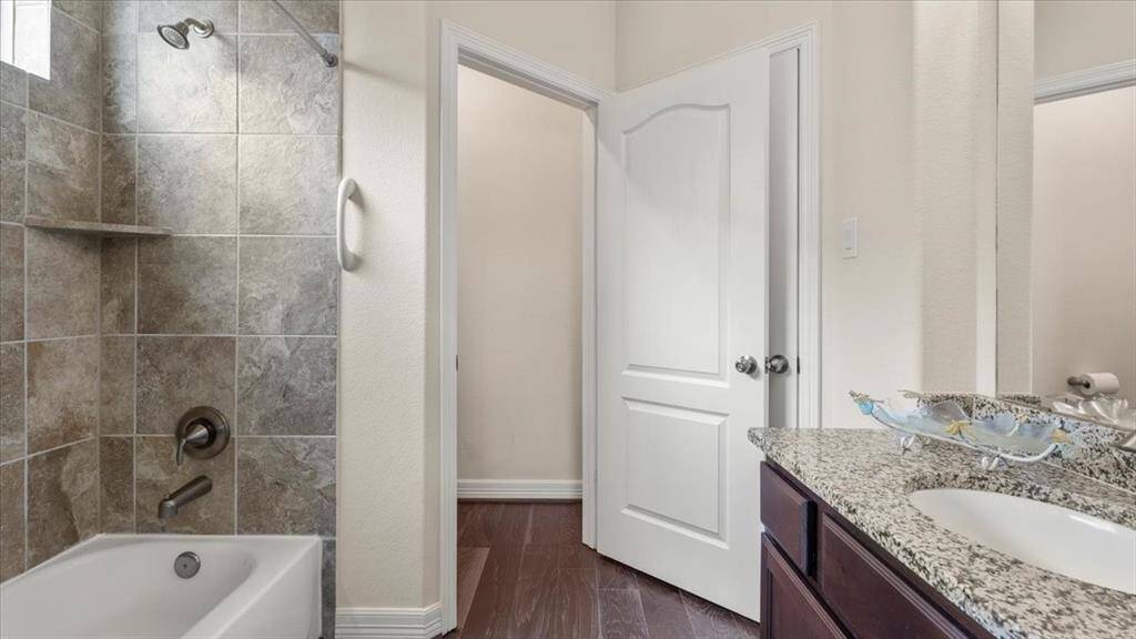 This bathroom features a tiled shower and tub combination, granite countertop with a built-in sink, and dark wood cabinetry. The space is well-lit and has a neutral color palette, creating a clean and modern look.