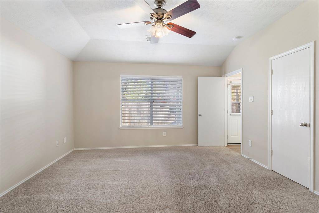 The primary bedroom has a vaulted ceiling, neutral paint, carpet and ceiling fan.