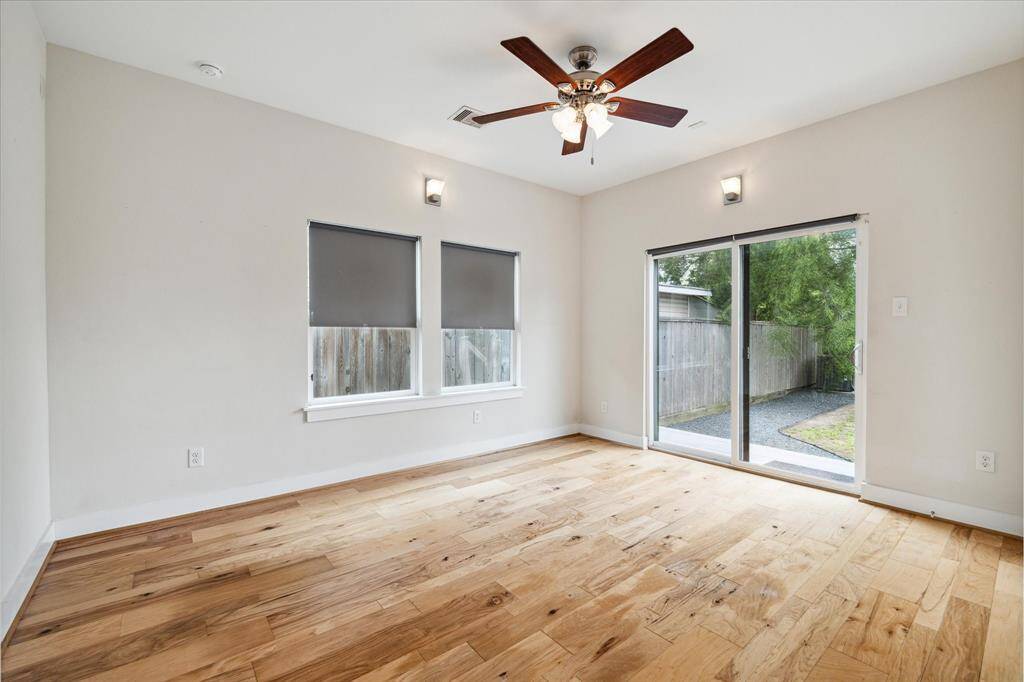 Bright room with hardwood floors, a ceiling fan, and sliding glass doors leading to a backyard. Ideal for a bedroom or living area, offering natural light and outdoor access.