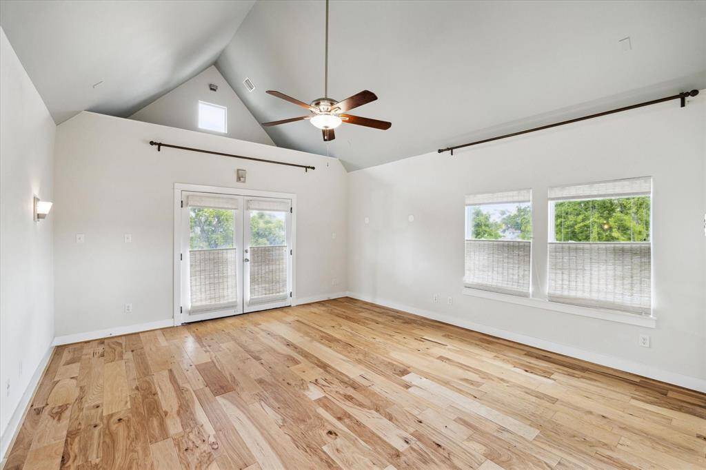 Bright, spacious room with vaulted ceiling, hardwood floors, and a ceiling fan. Features large windows and glass doors leading to an outdoor area, offering plenty of natural light.