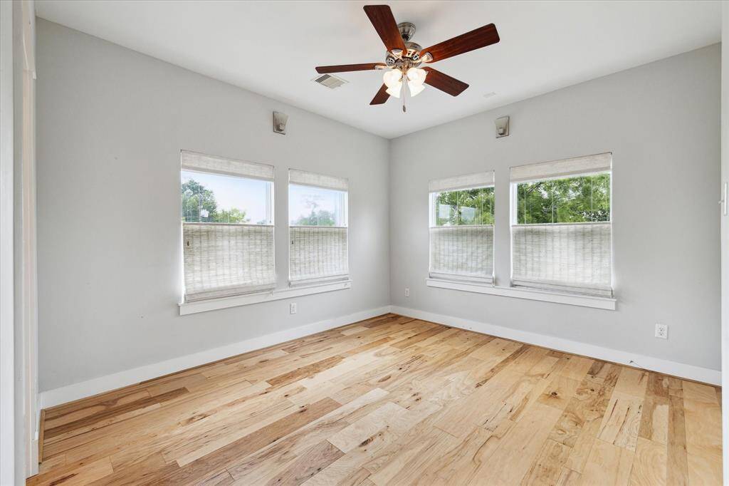 Bright bedroom with light wood flooring, neutral walls, and a ceiling fan. Multiple windows provide ample natural light.