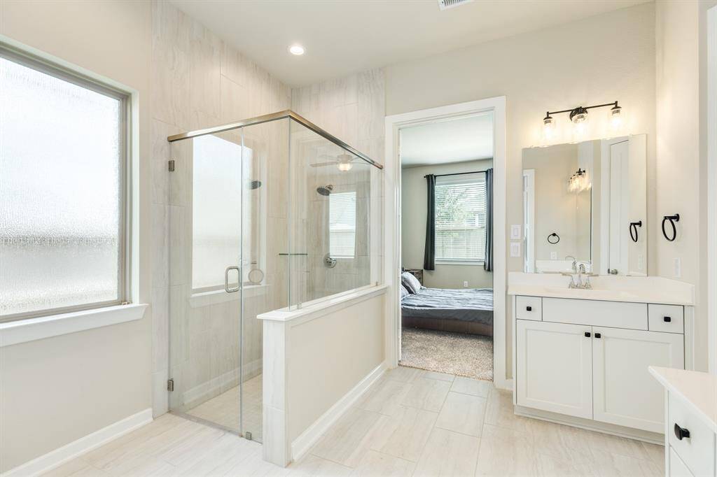 The primary bathroom has a walk-in glass shower The vanity mirrors  providing both classic and modern aesthetics.
