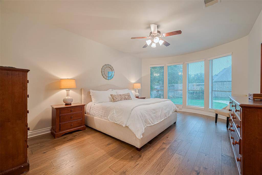 The serene primary bedroom features beautiful wood floors, a calming neutral palette, a ceiling fan for comfort, and a stunning bay window that overlooks your expansive backyard