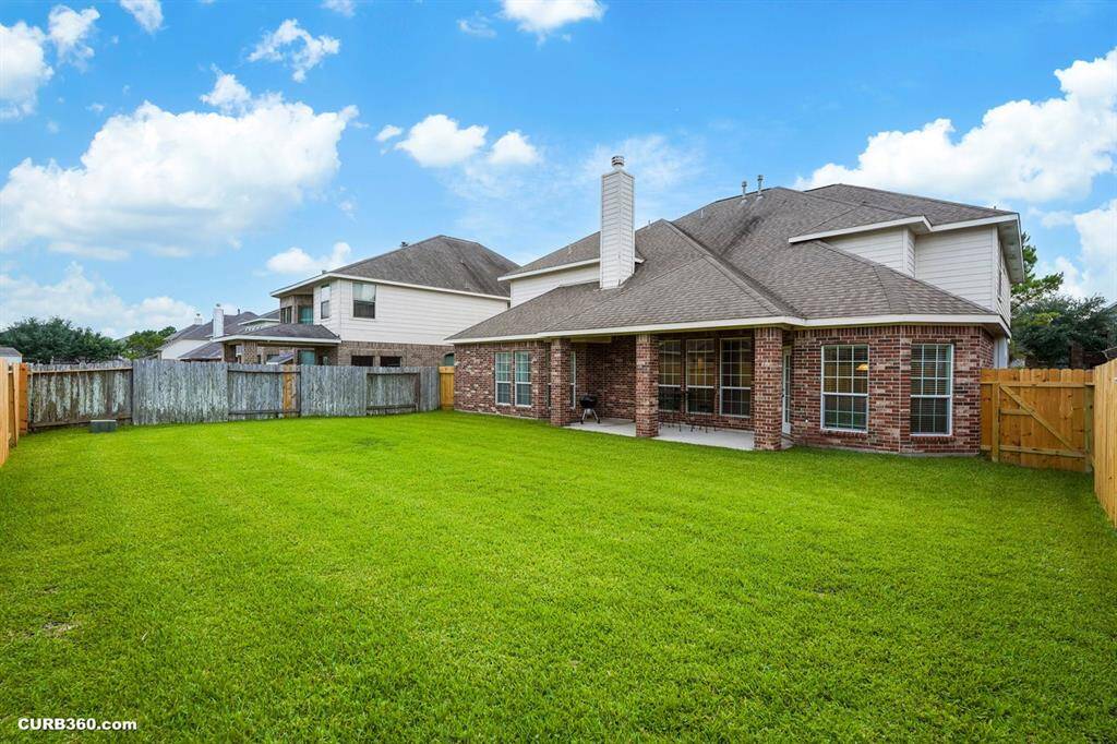 spacious backyard with a well-maintained lawn, a covered patio, and a brick exterior