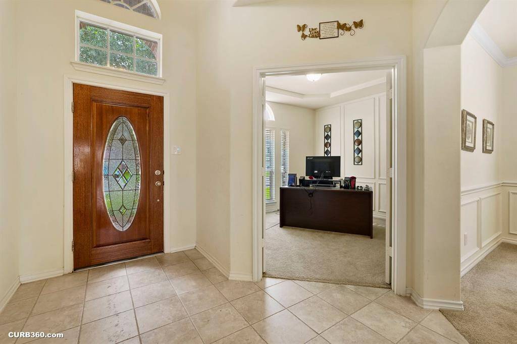 inviting entryway with a decorative glass front door and tiled flooring. Adjacent is a cozy office or study space