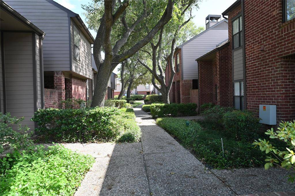 The sidewalk in front of Unit 80 is shaded by large trees and lush bushes.