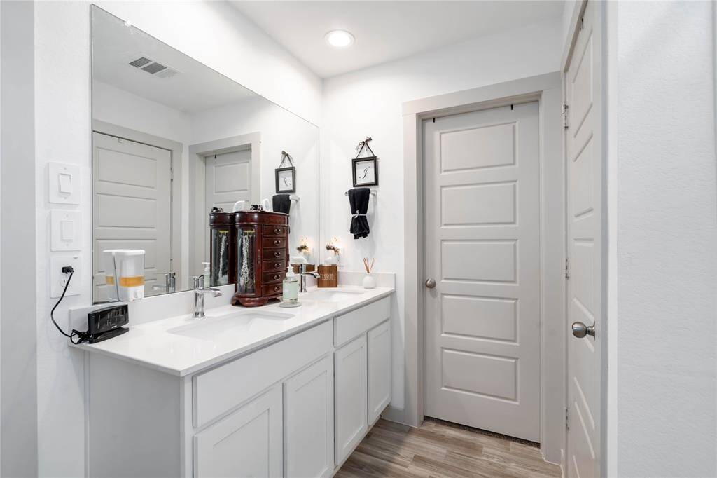 Spacious primary bathroom featuring dual sinks, sleek quartz countertops, and ample storage with white cabinetry.