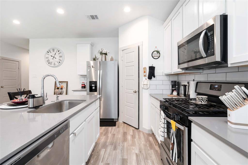 Stylish kitchen boasts quartz countertops, stainless steel appliances, white cabinetry, and a pass-through bar for easy entertaining.